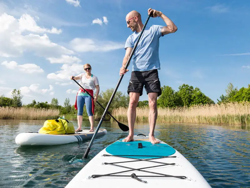 A man and a woman stand up paddle boarding on a lake