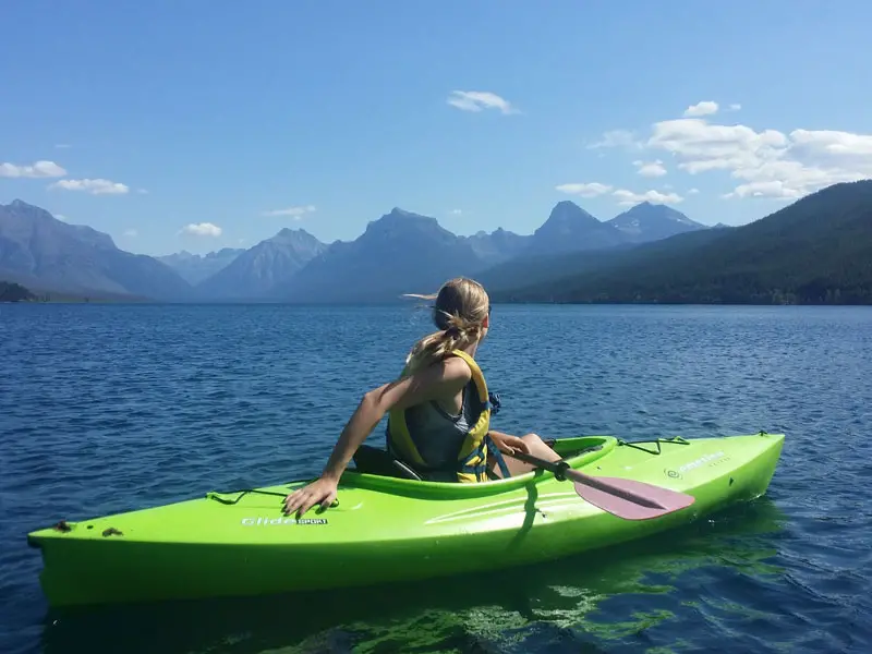 A woman sitting in a recreational kayak on a lake looking at mountains