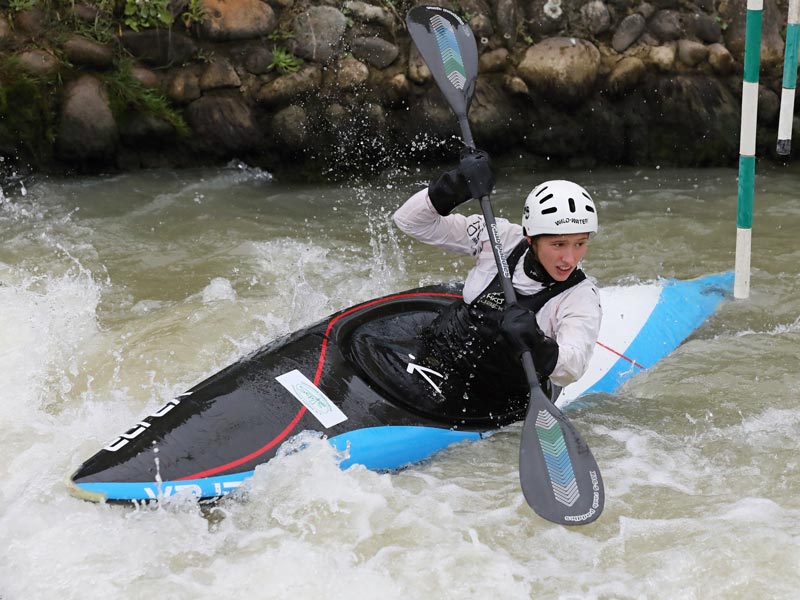 A person paddling a white-water kayak down a slalom course in a raging river.