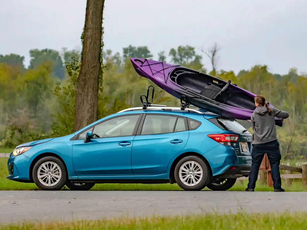 A person loading a kayak onto a car roof rack.