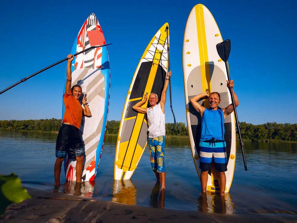 three men holding SUP boards