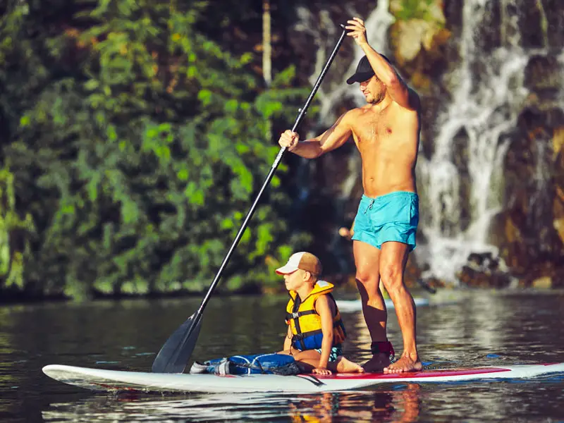 A man and young son paddle boarding in the sun
