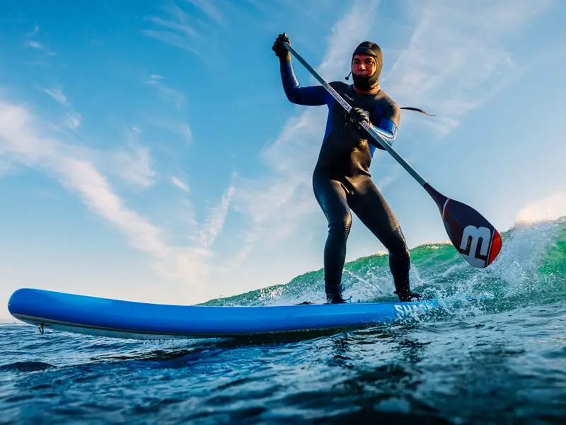 A man wearing wetsuit, glove, and hood 
SUP surfing in cold water