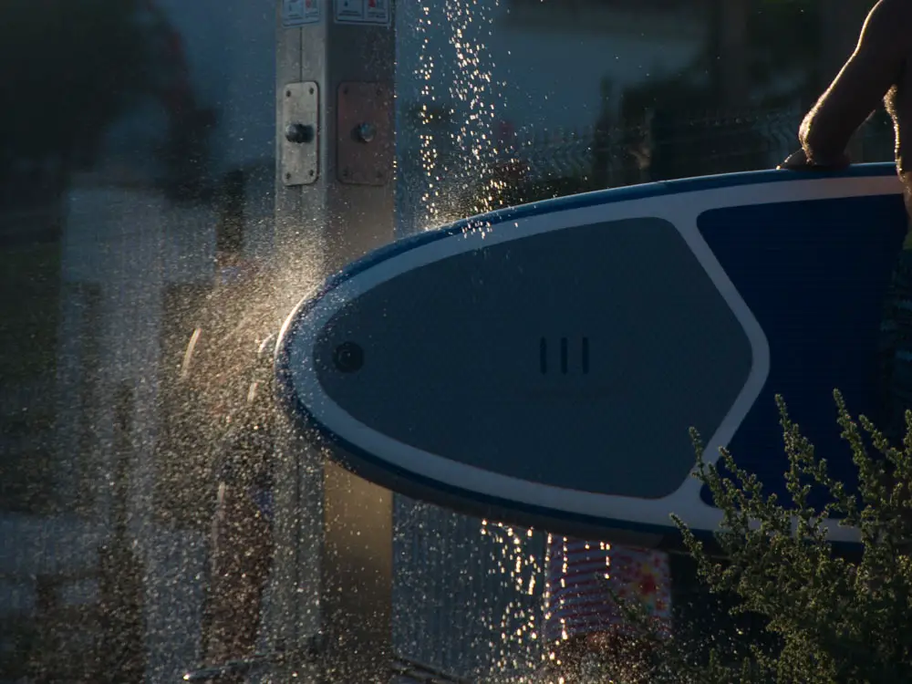 A man washes an inflatable paddle board with a beach shower