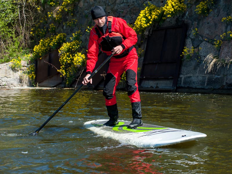A man paddle boarding down a river wearing a drysuit and life jacket