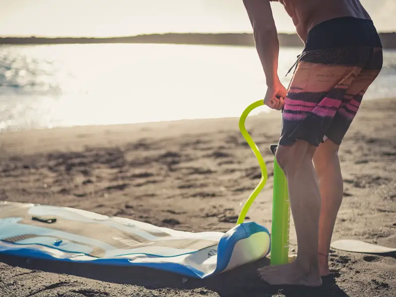 A man inflating an inflatable paddle board on the beach.