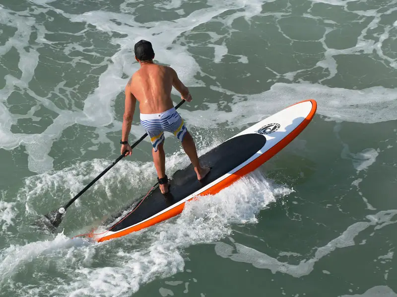 A man riding a SUP Surf paddle board. One of the types of paddle boards.