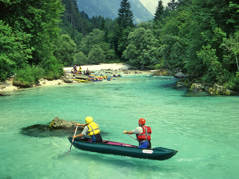 two men canoeing down a river wearing life jackets and helmets.
