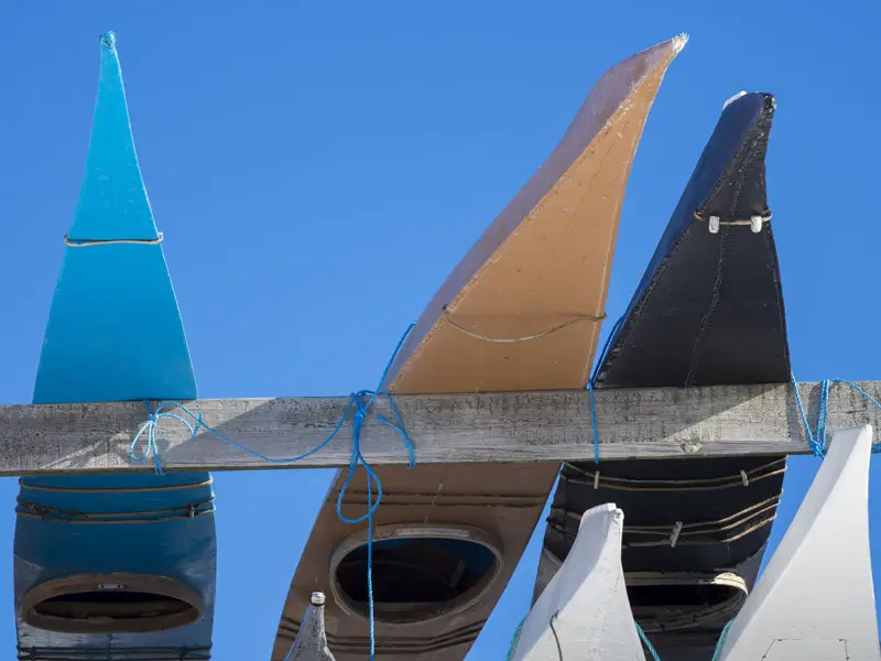 Three traditional Greenland kayaks stored on a rack