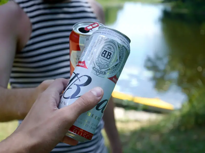 Two friends holding beers with a kayak in the background