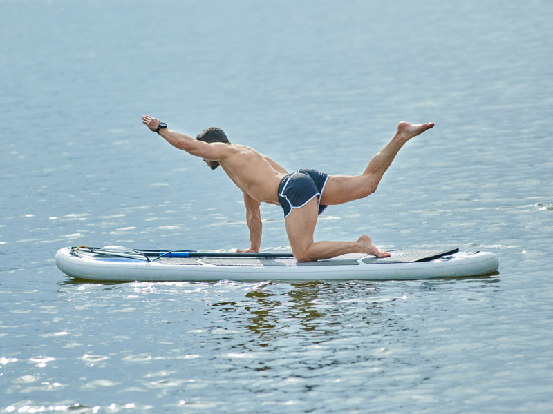 A muscular man working out on a paddle board.