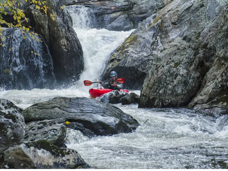 A man whitewater kayaking down a raging river with waterfalls