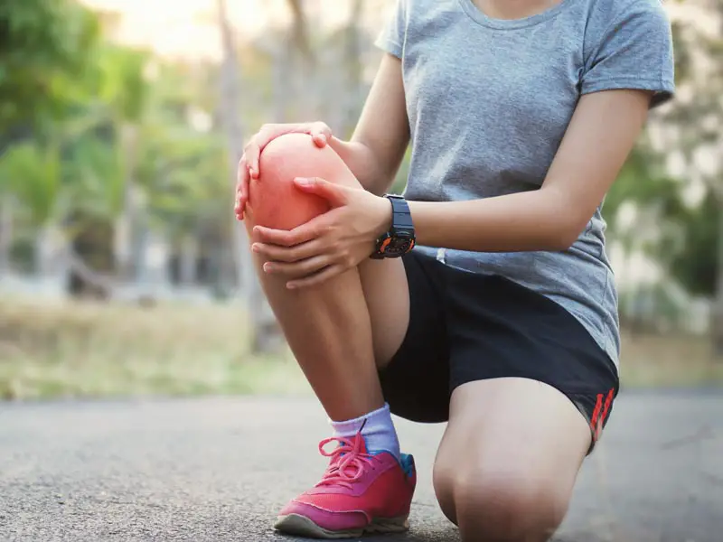 A woman runner holding her sore knee because of pain caused by running.