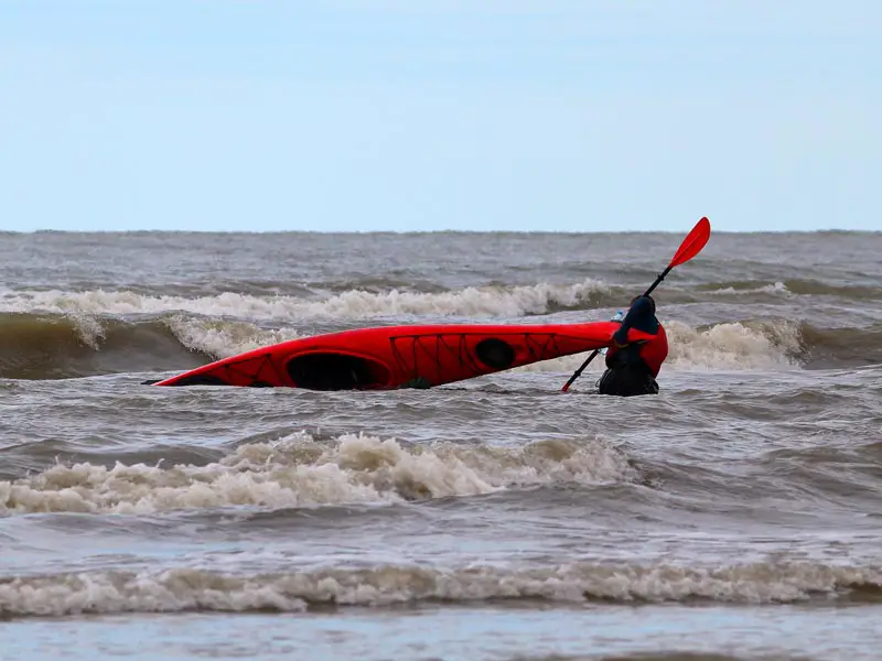 A kayaker pulls an overturned kayak out of the surf in rough weather.