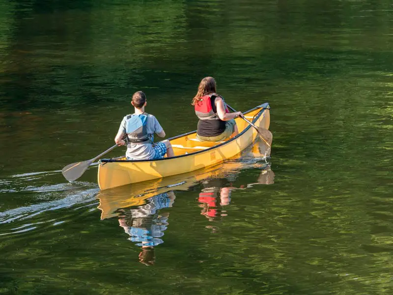 Two people, a couple, paddling a recreational canoe down a sedate, slow moving river.