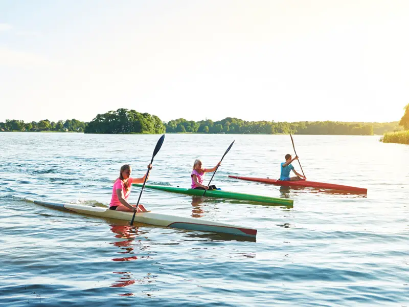 Three people paddling racing kayaks across a still lake. racing kayaks are very slim and close to the water.